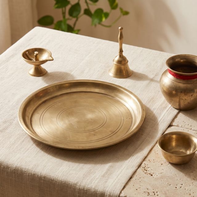 A brass thali, diya, bell, kalash and bowl on a cotton cloth.