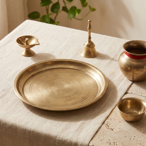 A brass thali, diya, bell, kalash and bowl on a cotton cloth.