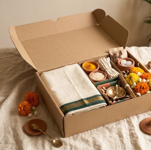 An open kraft gift box holding a folded cloth, flowers, a brass lamp and small bowls.